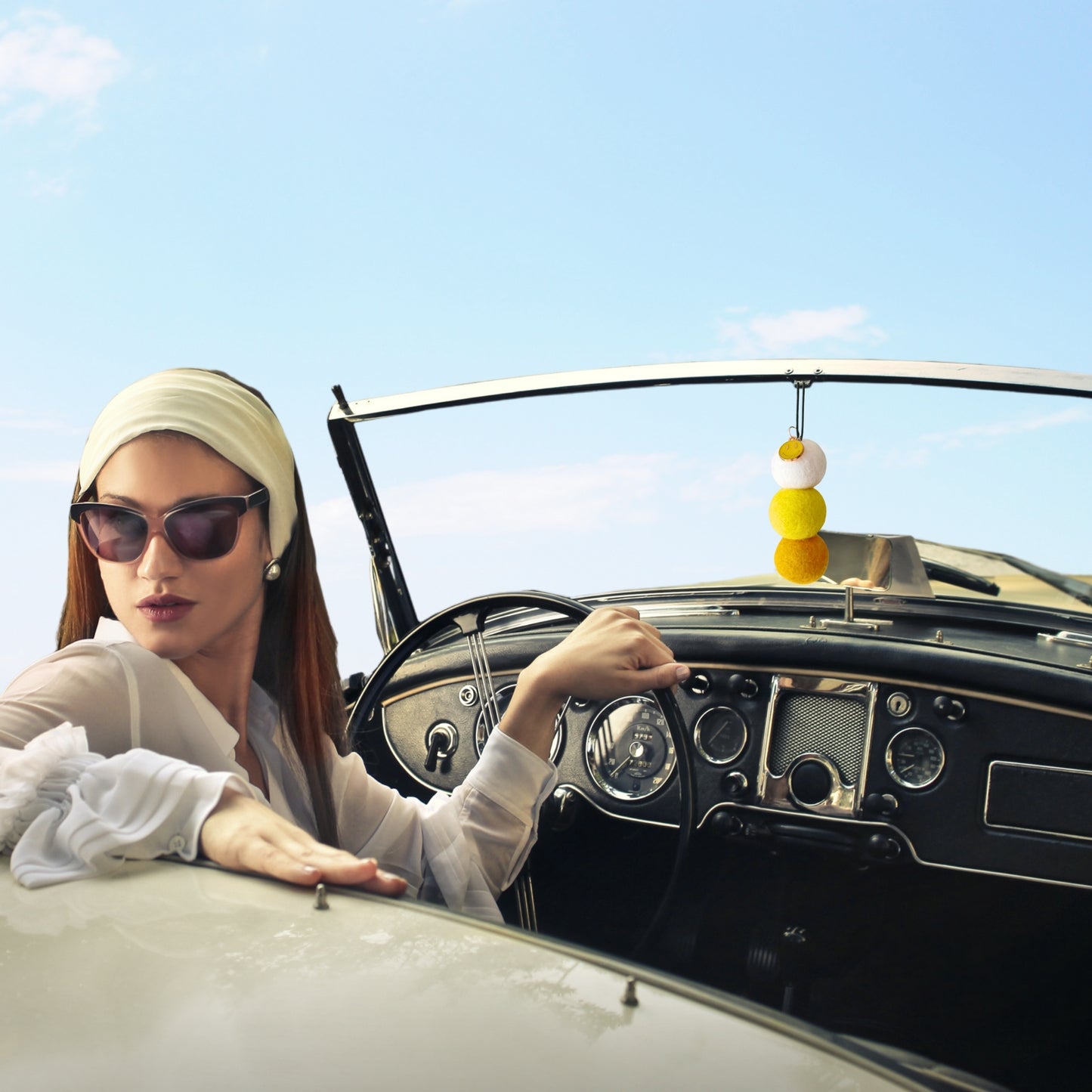Woman sitting in a vintage car with a clear blue sky background and hanging car diffuser