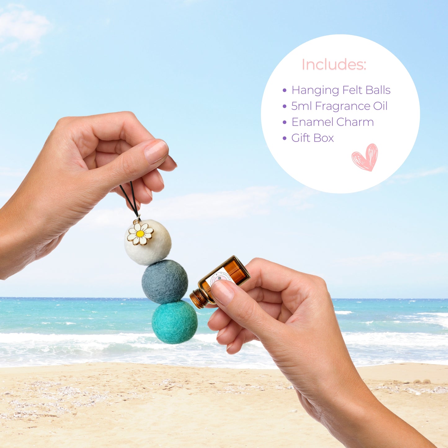 Hands applying Cherry Blossom oil to wool felt car diffuser with daisy charm, shown with included kit features like essential oil, gift box, and charm on beach background