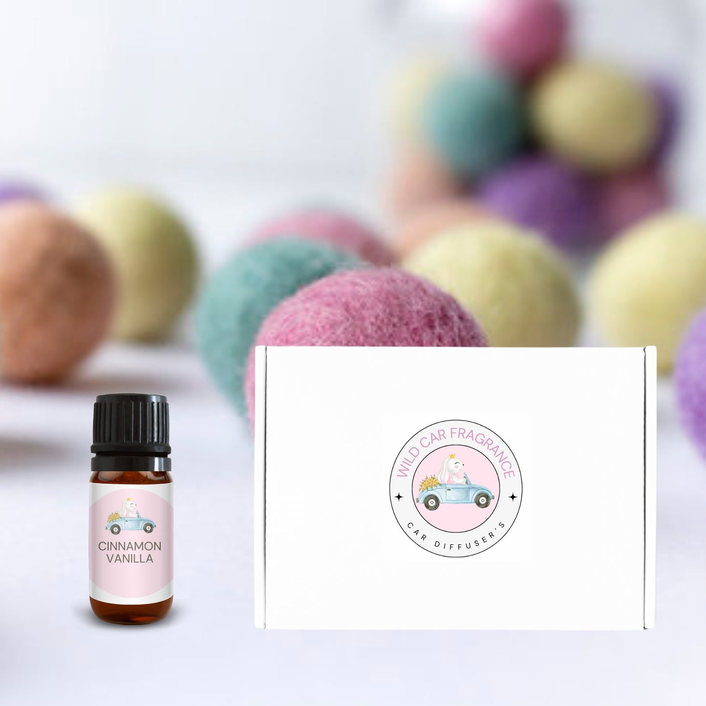 Cinnamon vanilla essential oil bottle and white gift box with logo, surrounded by pastel felt balls