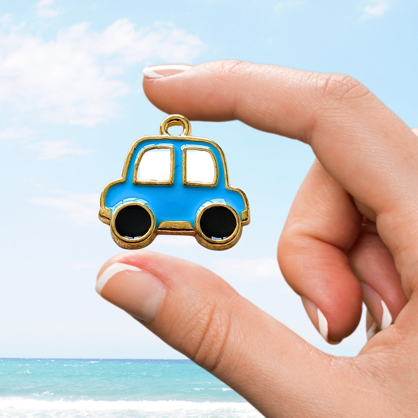 Hand displaying a blue enamel charm shaped like a cartoon car with gold accents.