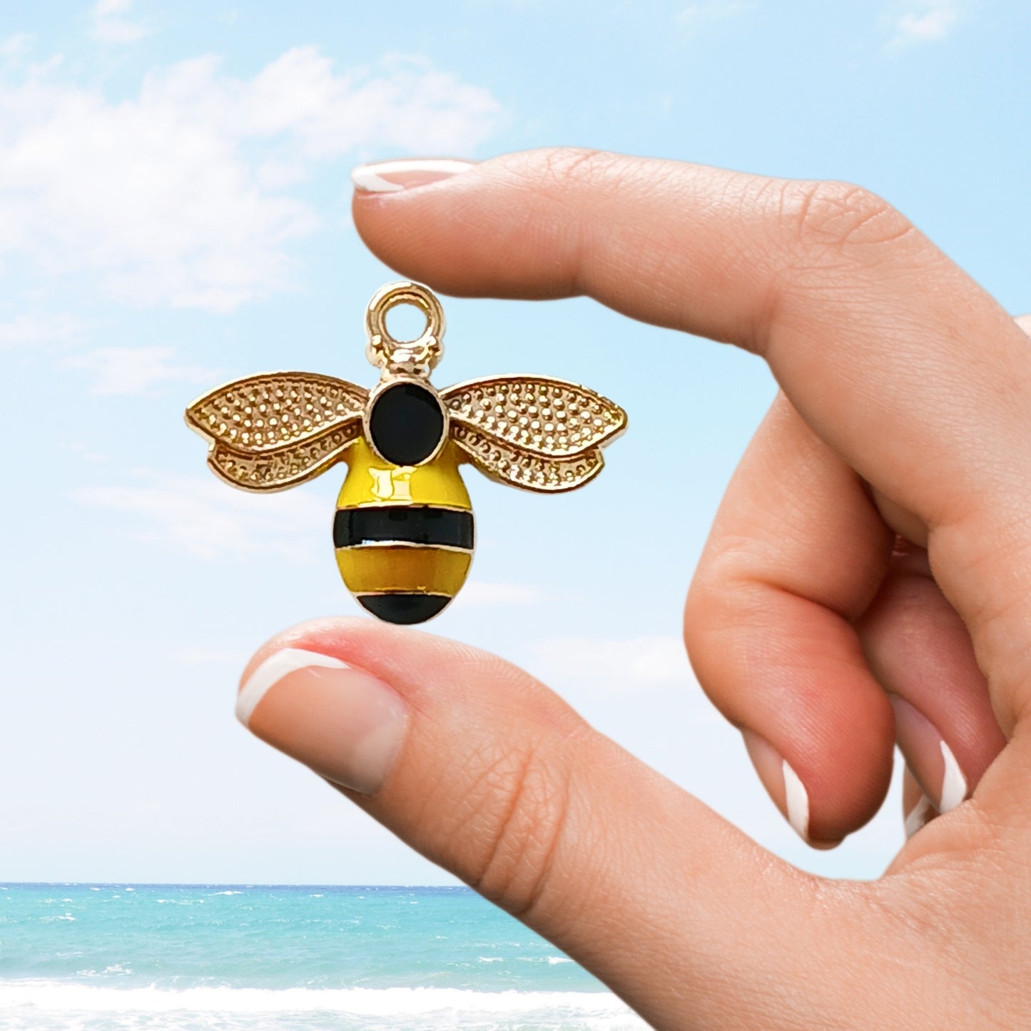Enamel bee charm with gold wings and yellow-black body held against a blue sky.