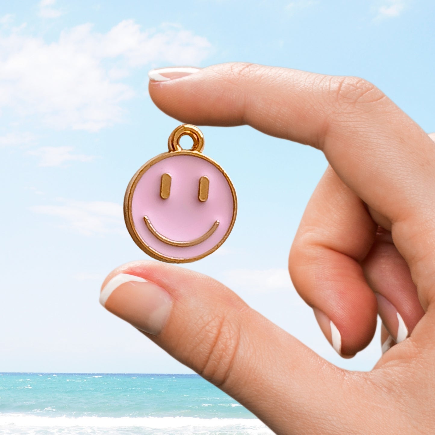 Hand showing a pink smiley face charm by the sea.