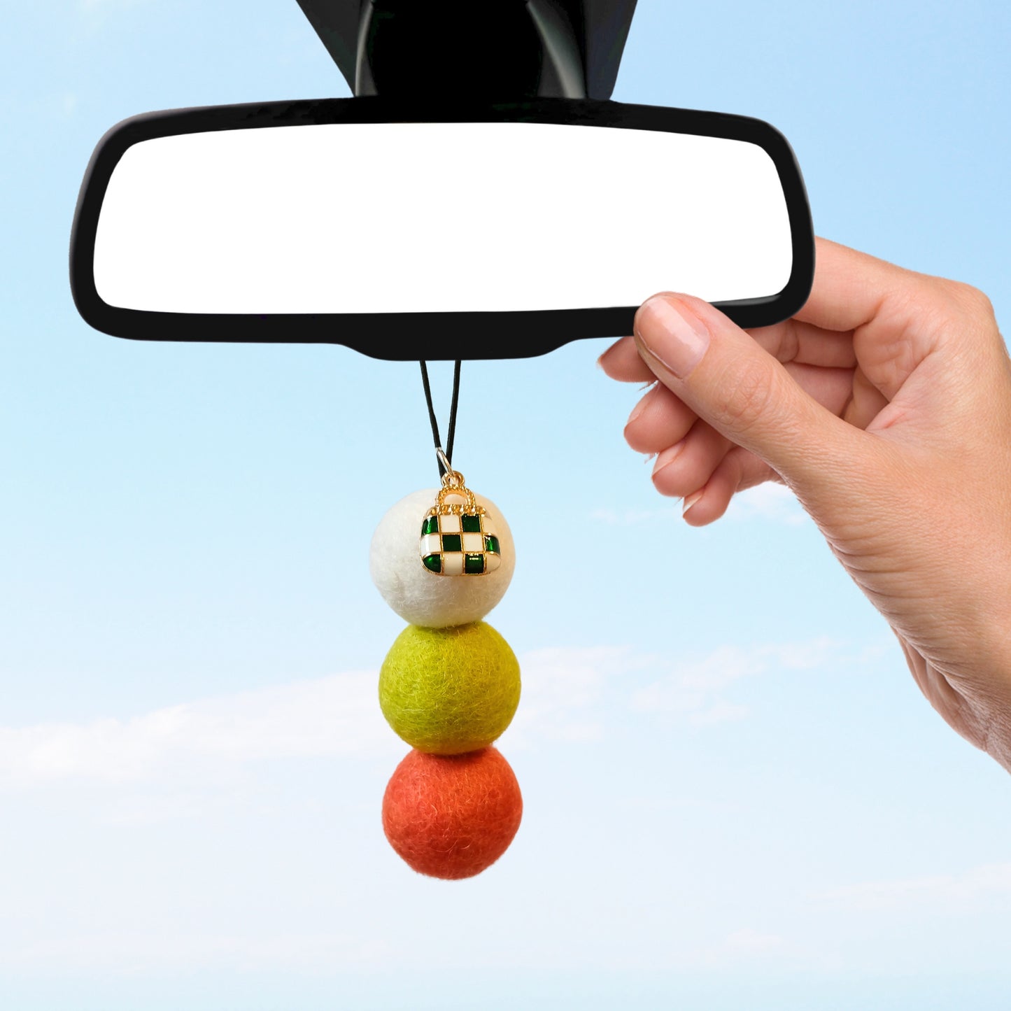 Hand hanging multicolour felt ball car diffuser with enamel handbag charm from rearview mirror, promoting a stylish and sustainable alternative to traditional car air fresheners