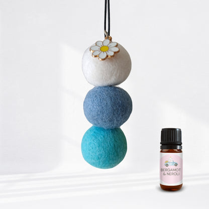 Stack of three felt balls hanging with a small bottle labeled 'Bergamot & Neroli' on a white background