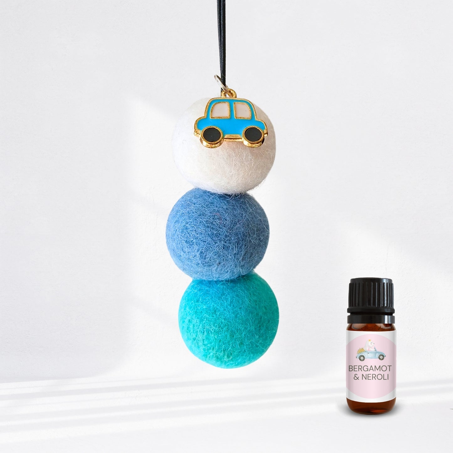Decorative hanging diffuser with blue and green balls and a small car charm, next to a bottle of essential oil labelled 'Bergamot & Neroli'.