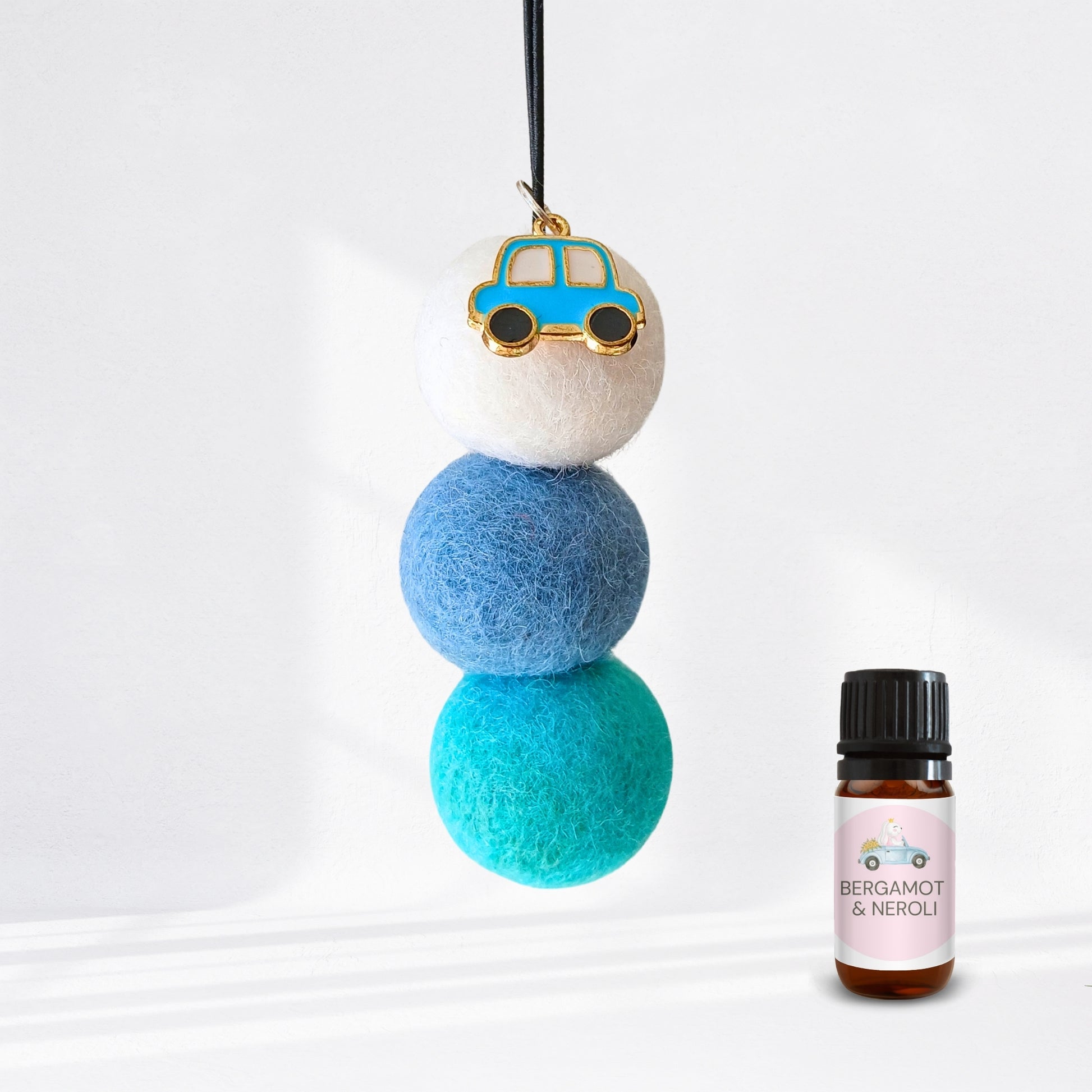 Decorative hanging diffuser with blue and green balls and a small car charm, next to a bottle of essential oil labelled 'Bergamot & Neroli'.