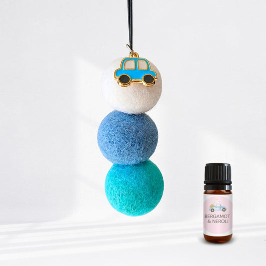 Decorative hanging diffuser with blue and green balls and a small car charm, next to a bottle of essential oil labelled 'Bergamot & Neroli'.