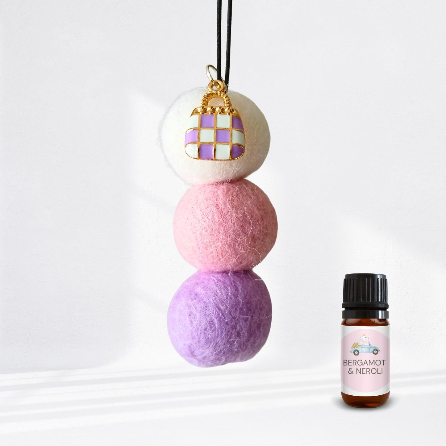 Three stacked felt balls with a keychain and a bottle of Bergamot & Neroli essential oil on a white background.