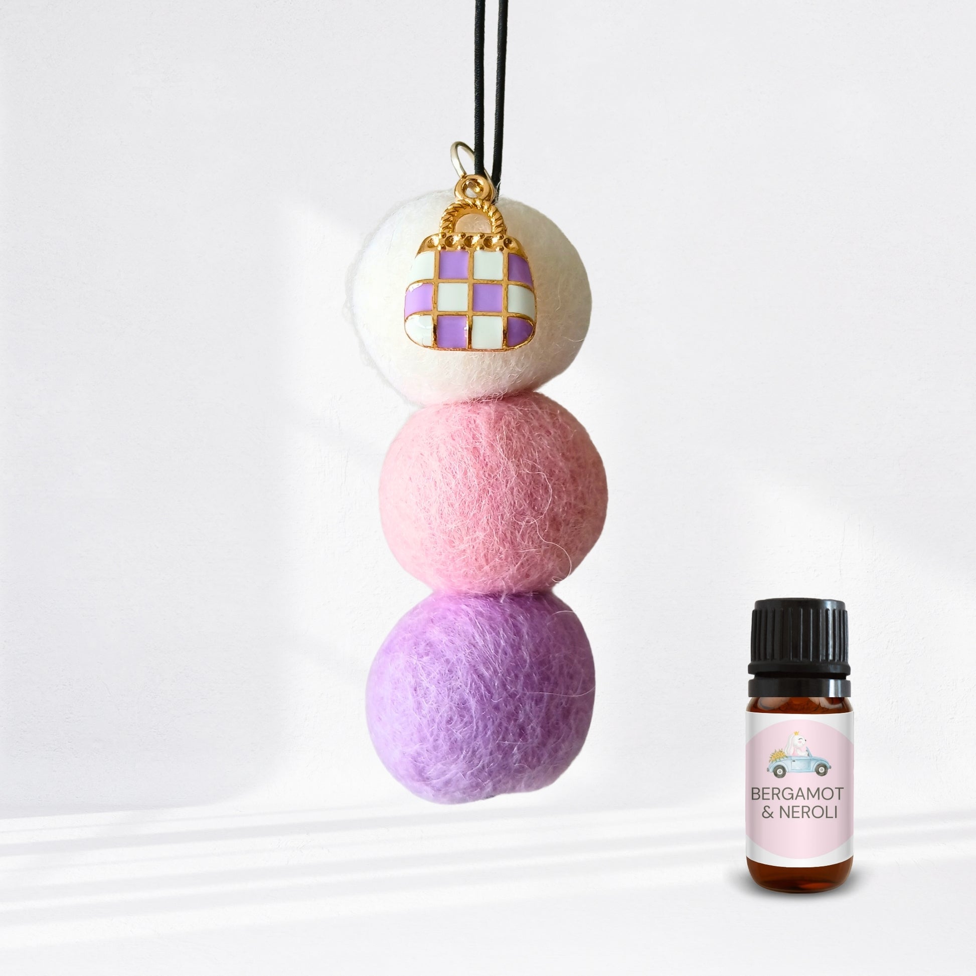 Three stacked felt balls with a keychain and a bottle of Bergamot & Neroli essential oil on a white background.
