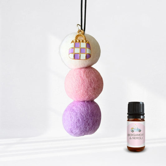 Three stacked felt balls with a keychain and a bottle of Bergamot & Neroli essential oil on a white background.