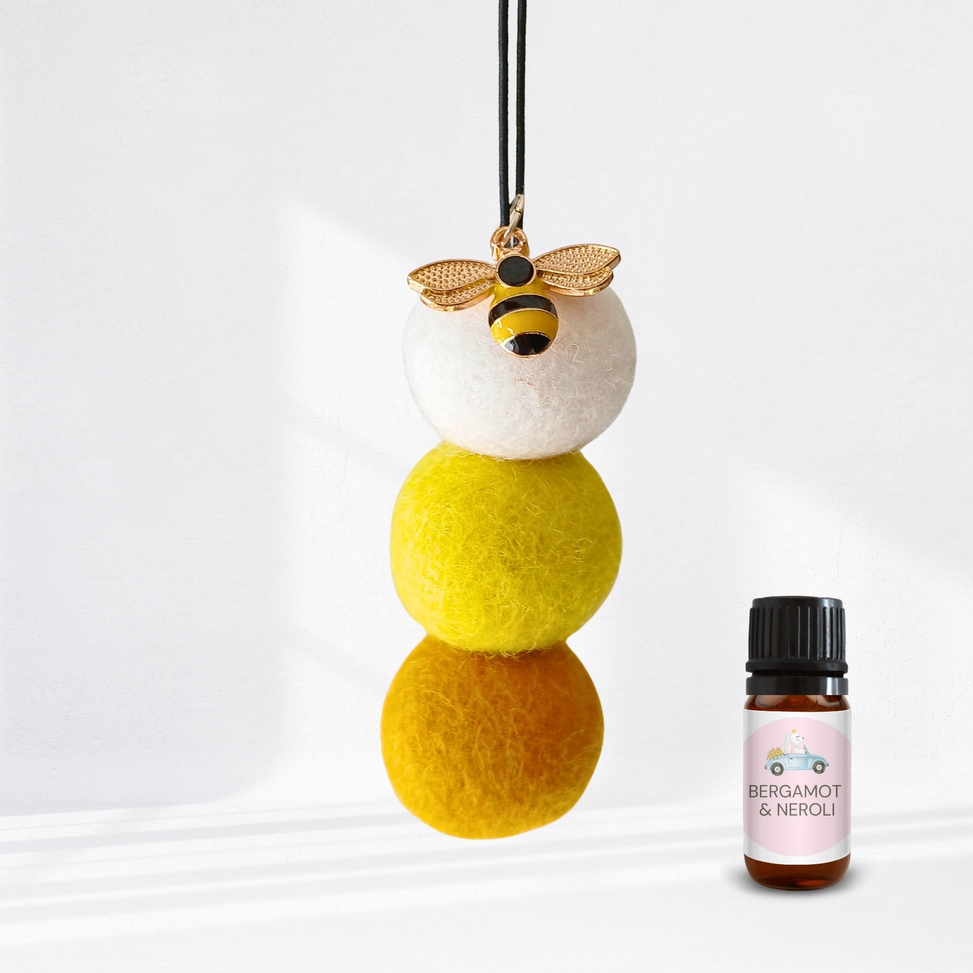 Decorative hanging ball with bee charm and a bottle of Bergamot & Neroli essential oil on a white background