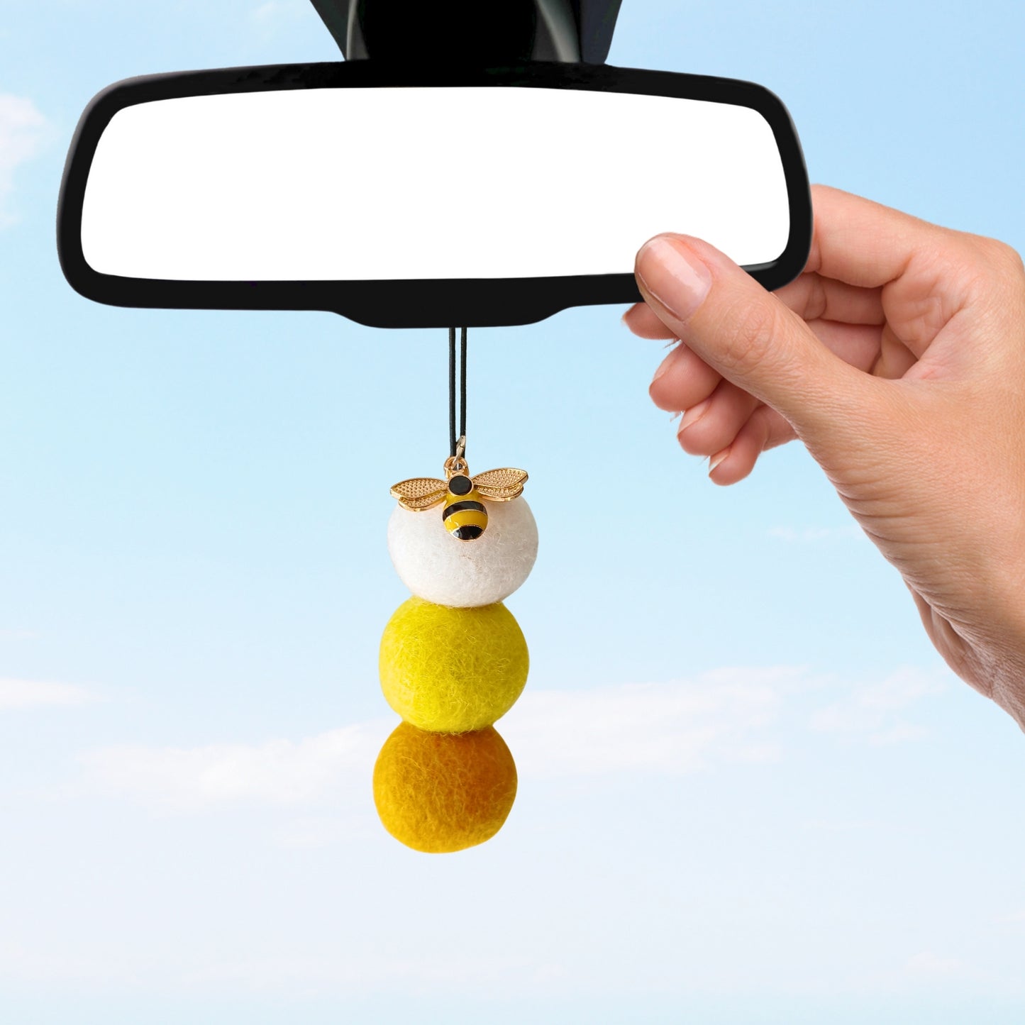 Hand holding a car hanging ornament with a blue sky background