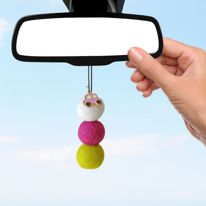 Colorful car charm hanging from a car mirror against a clear blue sky.