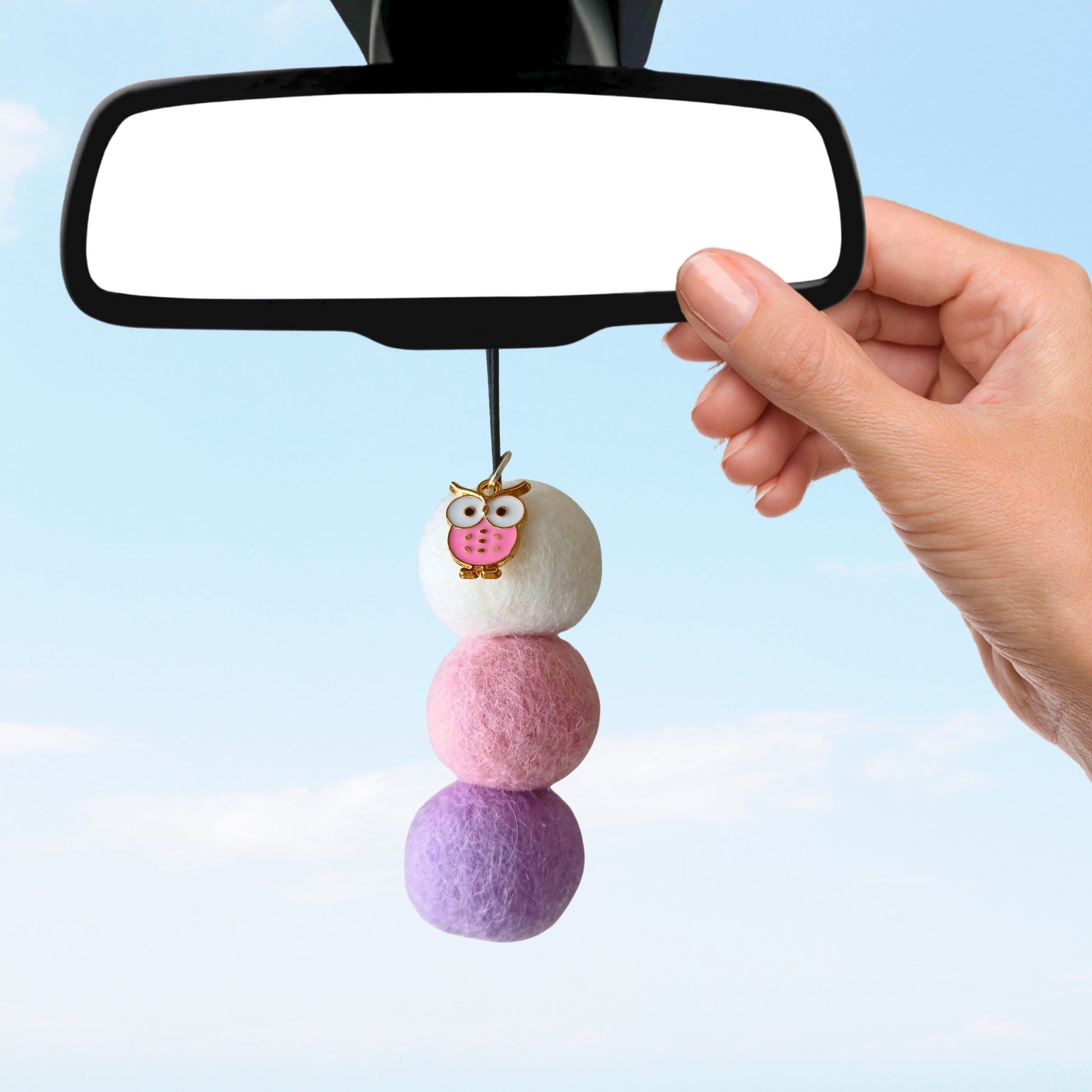 Pastel-colored car charm hanging from a car mirror against a light blue background