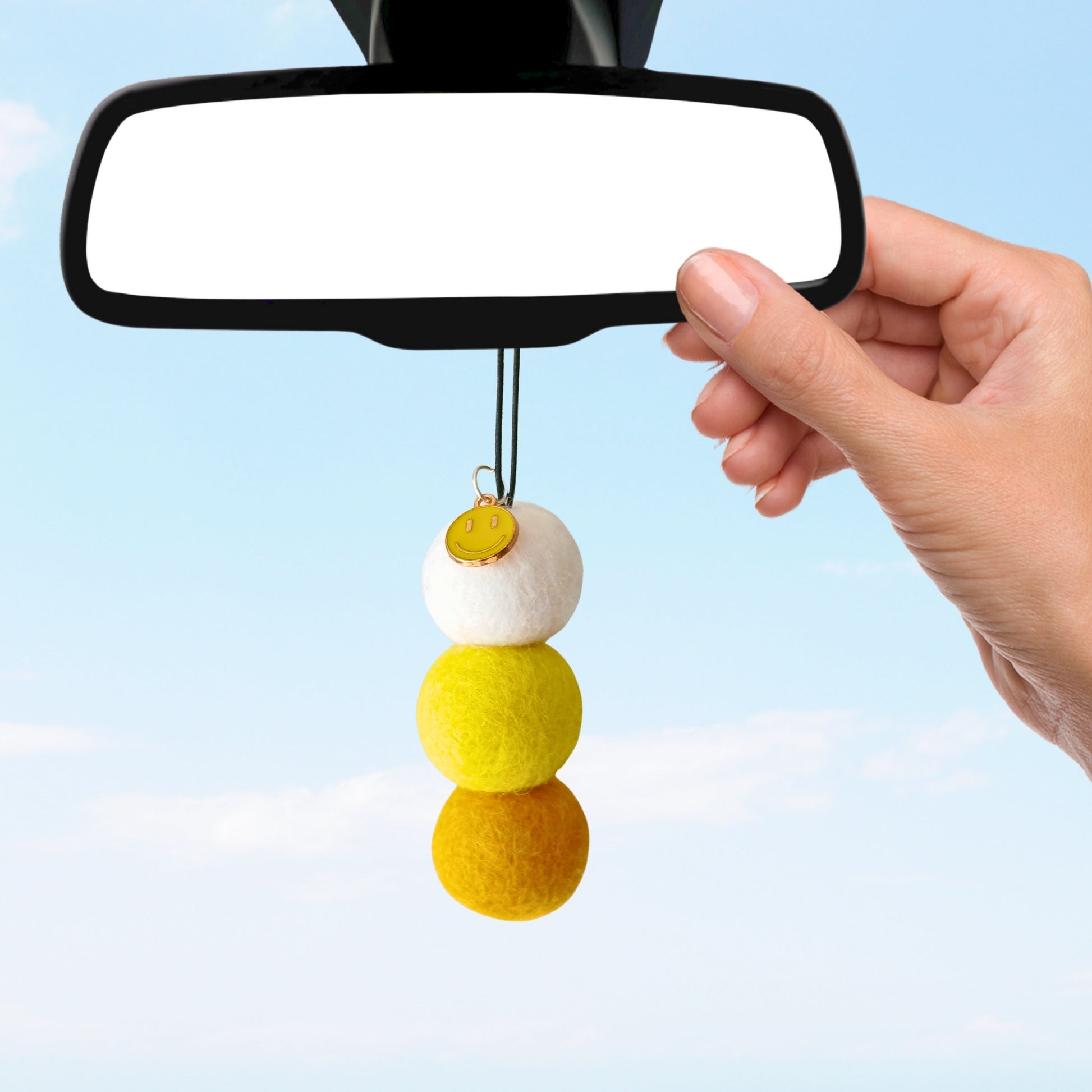 Car mirror with a decorative hanging charm against a clear blue sky