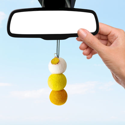 Car mirror with a decorative hanging charm against a clear blue sky