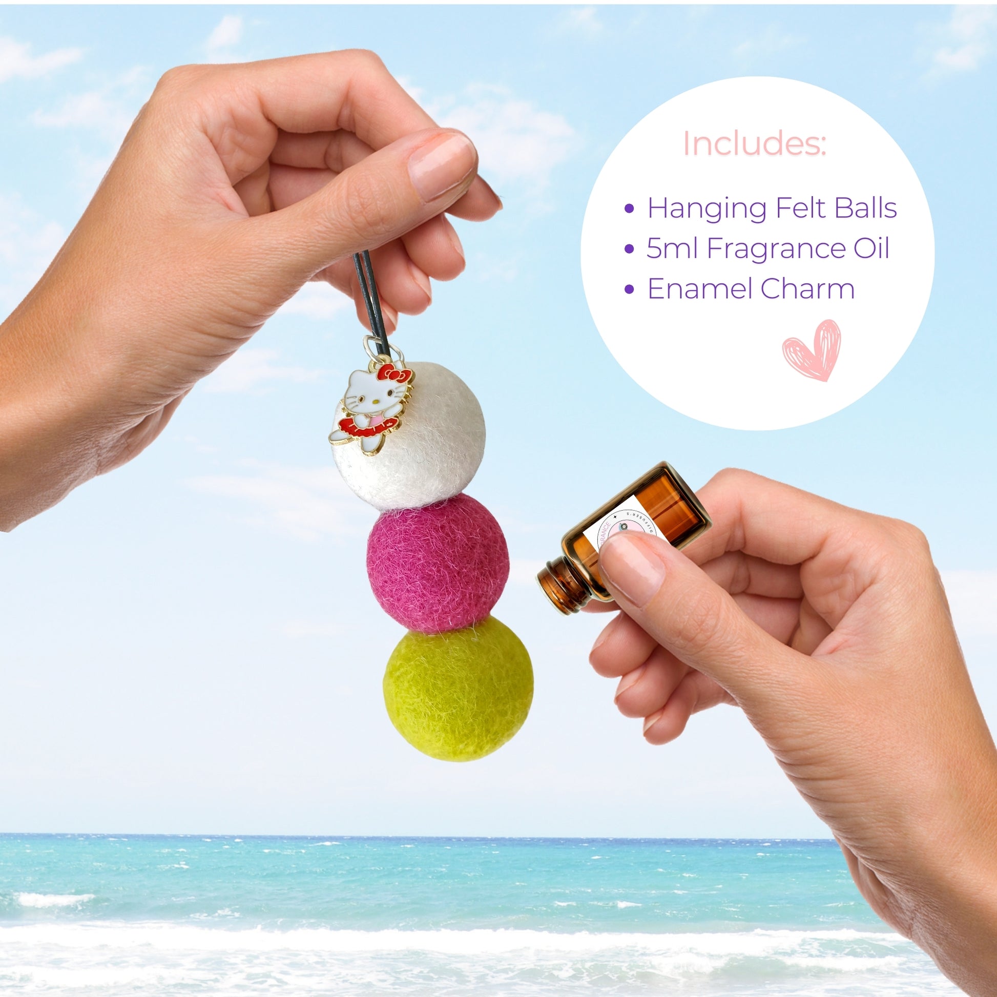 Colorful felt diffuser with hanging felt balls and a small bottle, held by hands against a beach background.