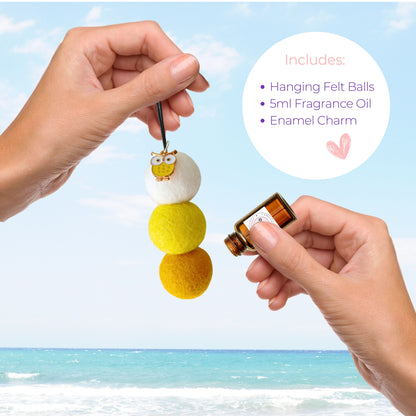 Hanging felt ball diffuser with fragrance oil and enamel charm against a beach background