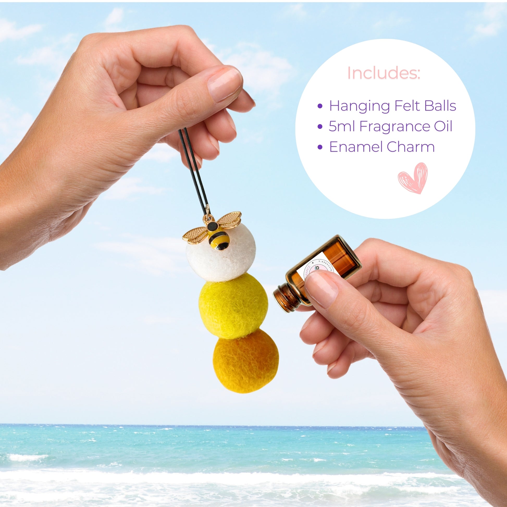 Hanging felt ball with fragrance oil and enamel charm held by a hand against a beach background