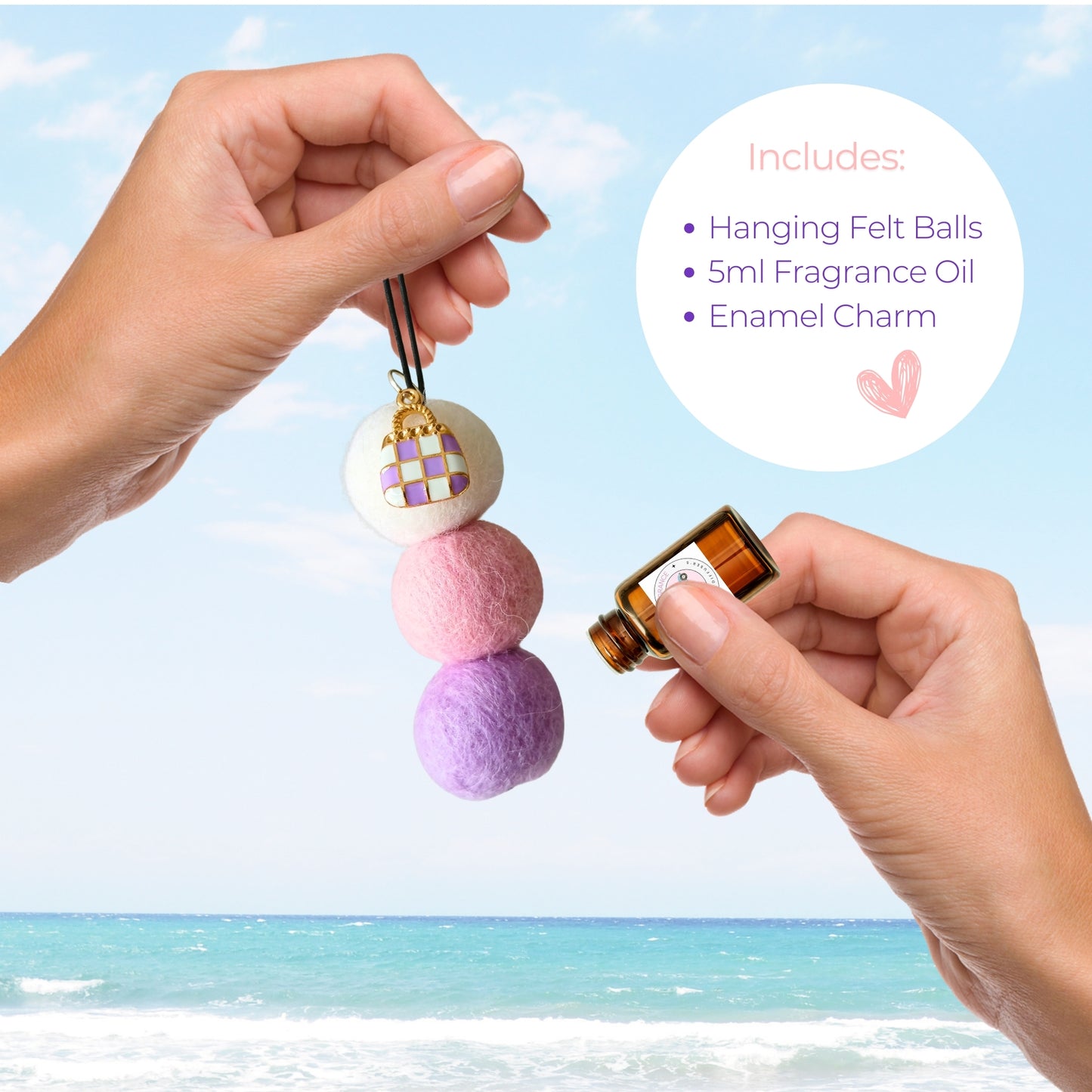 Hanging felt ball ornament with fragrance oil and enamel charm held by hands against a beach background.