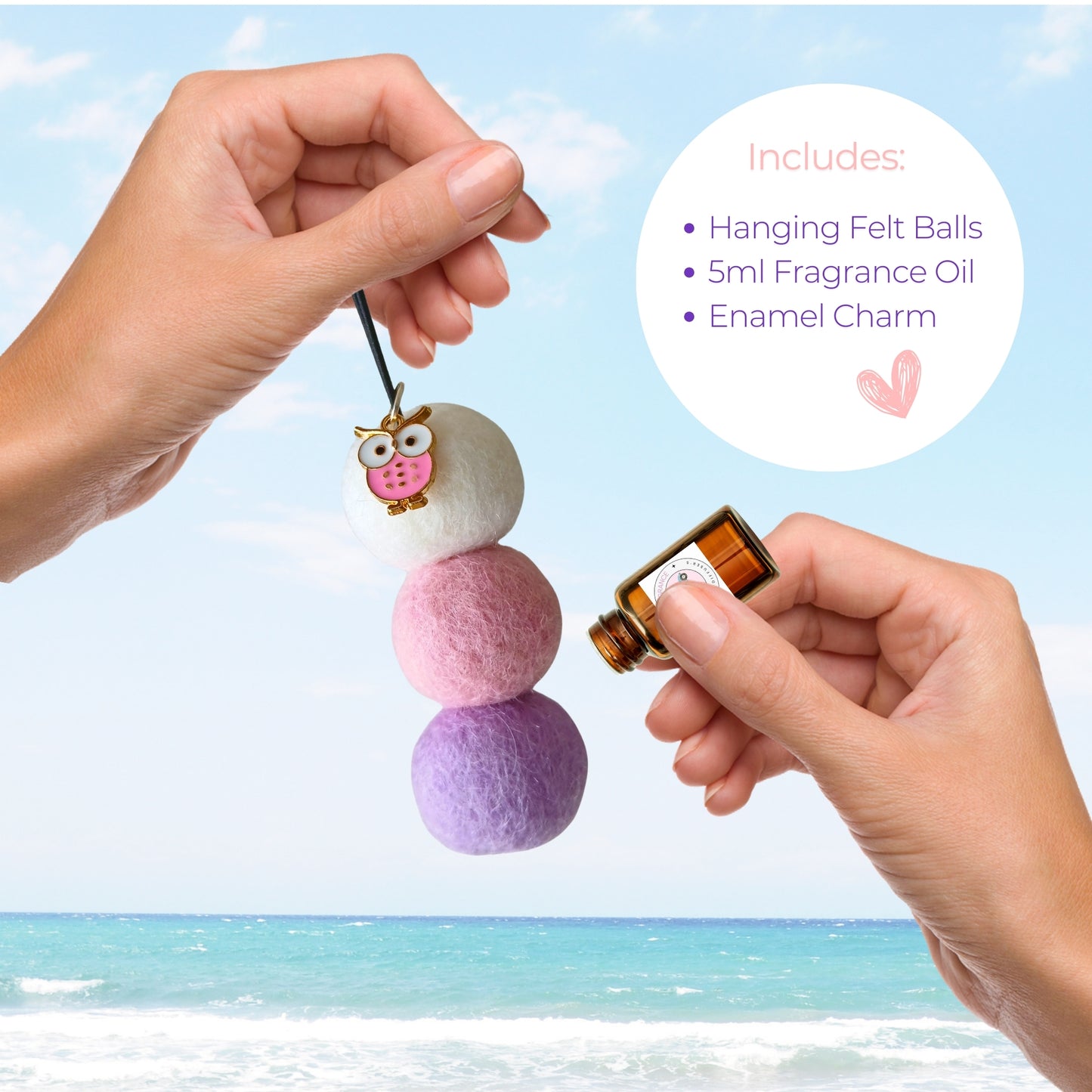 Hanging felt ball ornament with fragrance oil and enamel charm, held by a hand against a beach background.