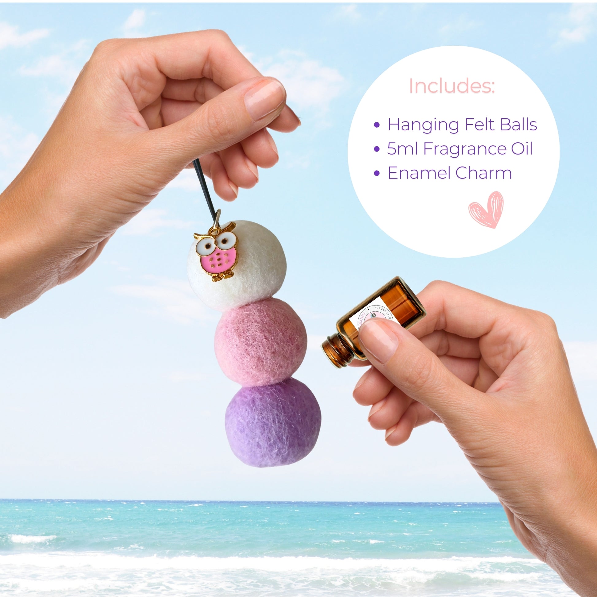 Hanging felt ball ornament with fragrance oil and enamel charm, held by a hand against a beach background.