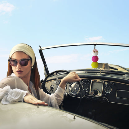Woman sitting in a vintage car with a colorful car accessory hanging from the rearview mirror.