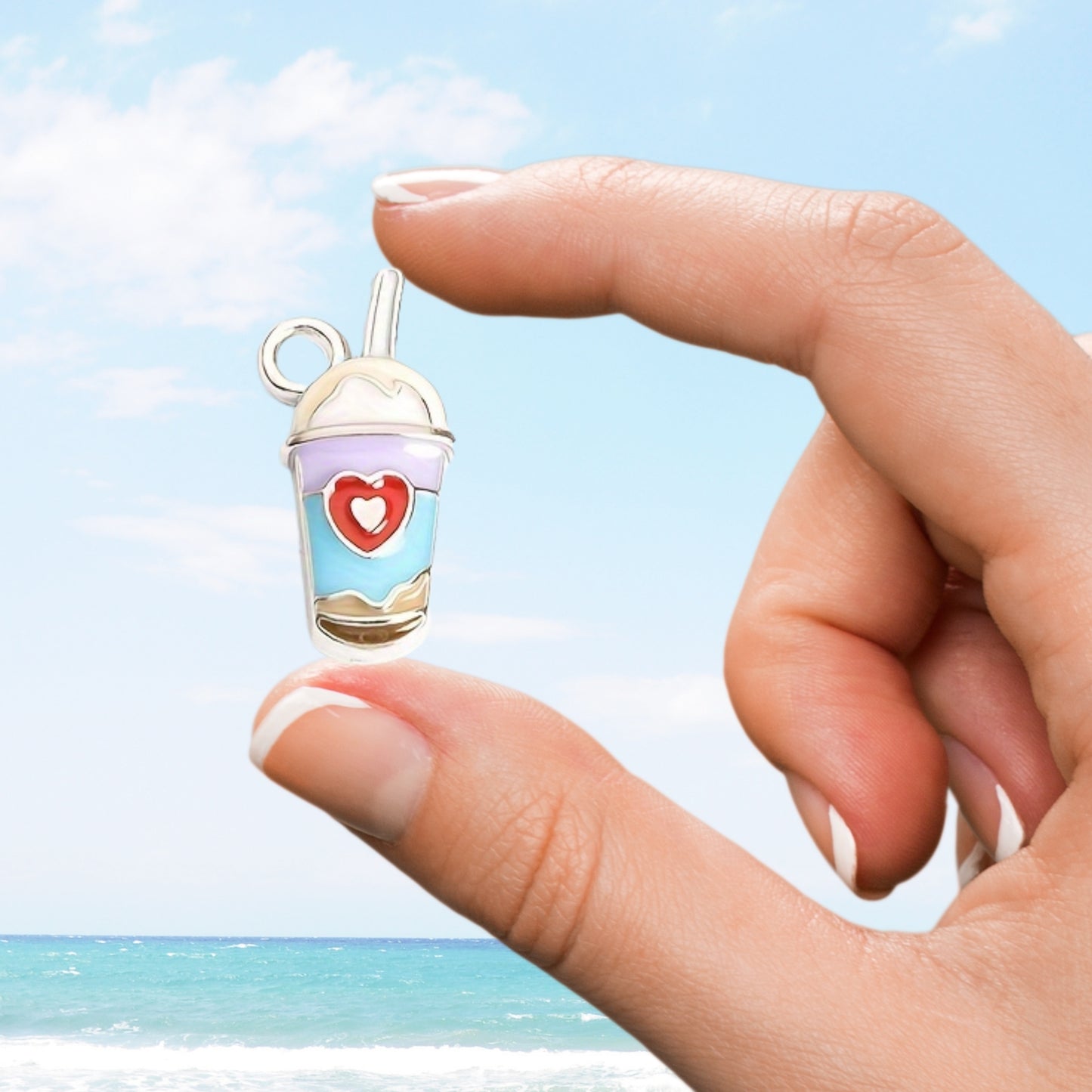 Hand holding a small cup-shaped charm with a heart design against a beach background