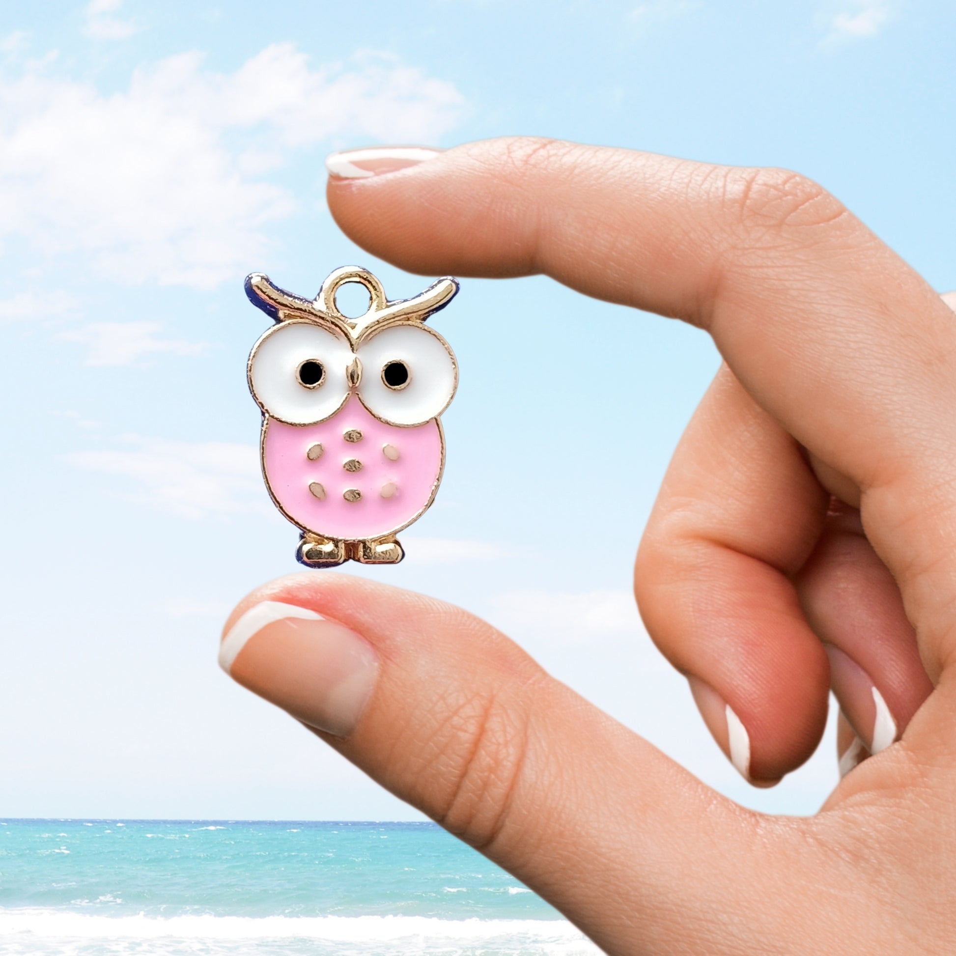 Hand holding a pink owl-shaped charm with a beach background