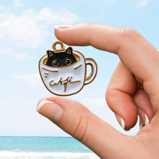 Hand holding a white coffee cup charm with a black cat peeking out and gold café script on the cup