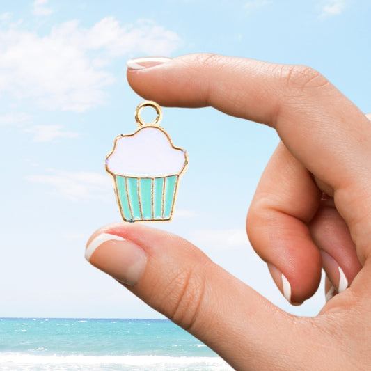 Hand holds mint blue cupcake charm with white icing over ocean view