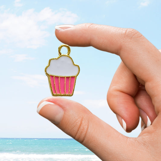 Hand holds pink cupcake charm with white icing above beach backdrop