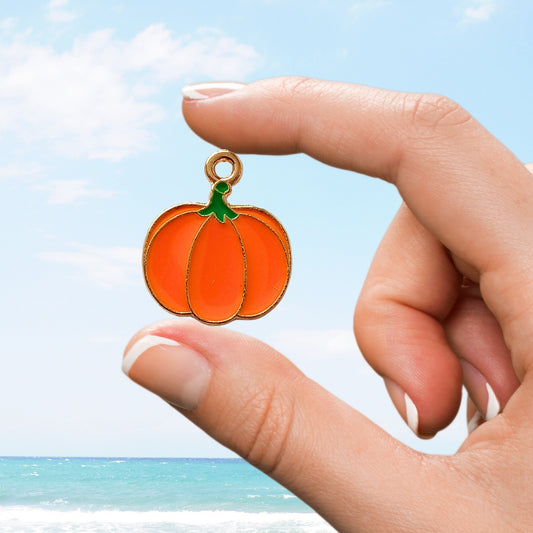 Hand holding a cute orange pumpkin charm with a green stem on a bright coastal day