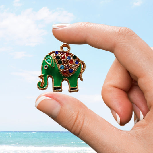 Hand holds green elephant charm with rainbow gem saddle near beach
