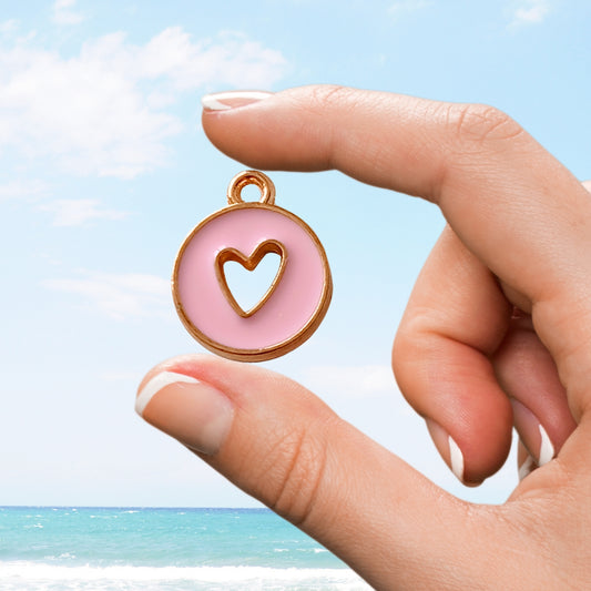Hand holds soft pink charm with heart cutout over ocean horizon