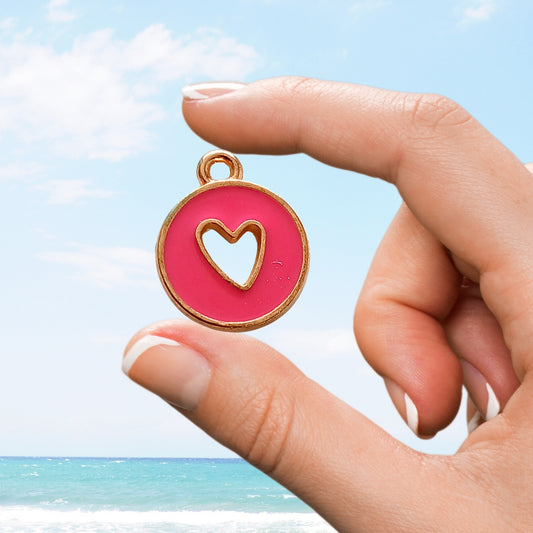 Hand holds bright fuchsia charm with heart cutout against blue sky