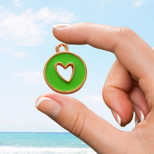 Hand holds vibrant green charm with cut-out heart design by ocean