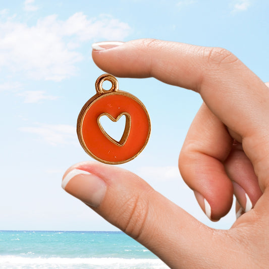 Hand holds round orange charm with heart-shaped cutout at seaside