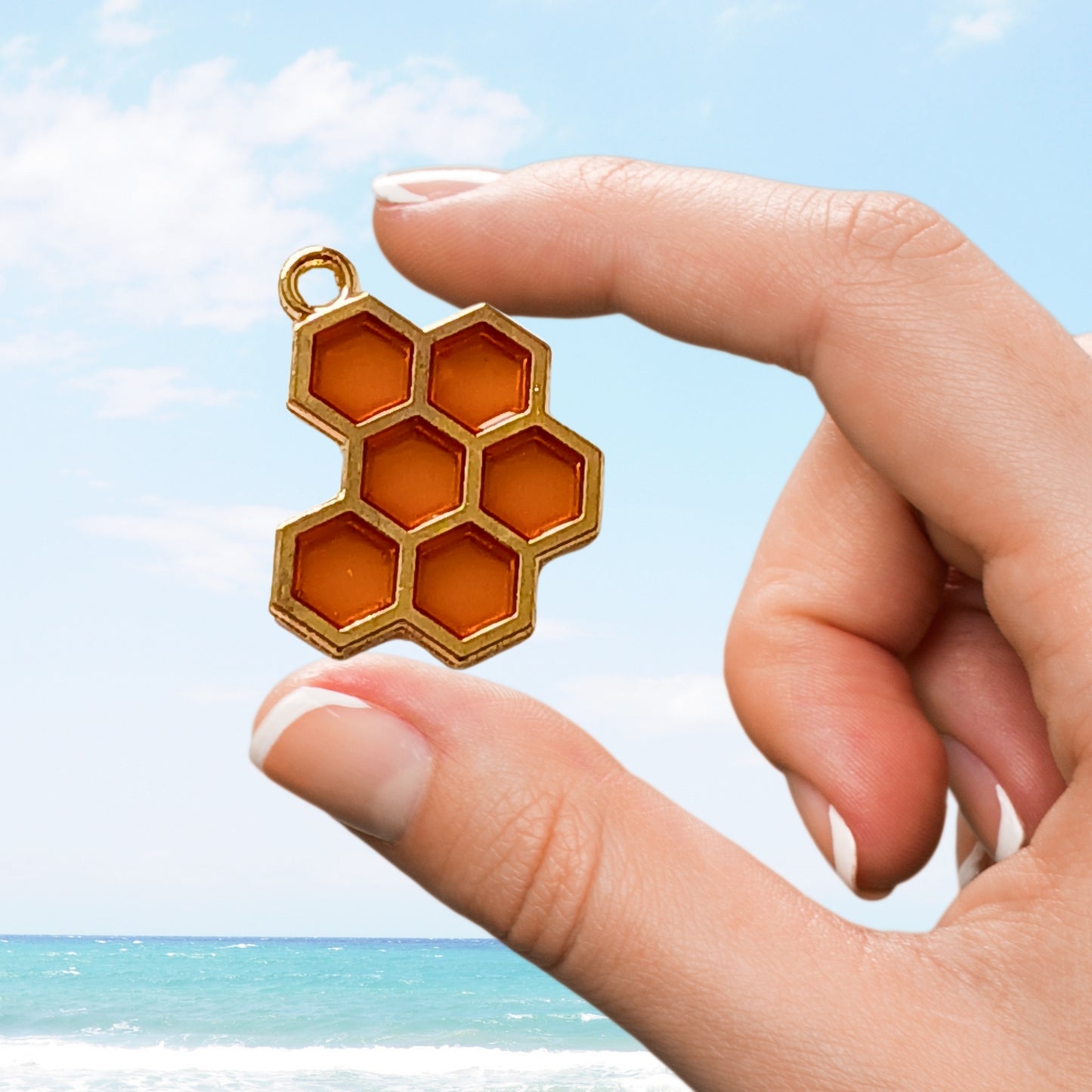 Orange honeycomb-shaped charm with gold edges held in front of beach backdrop.
