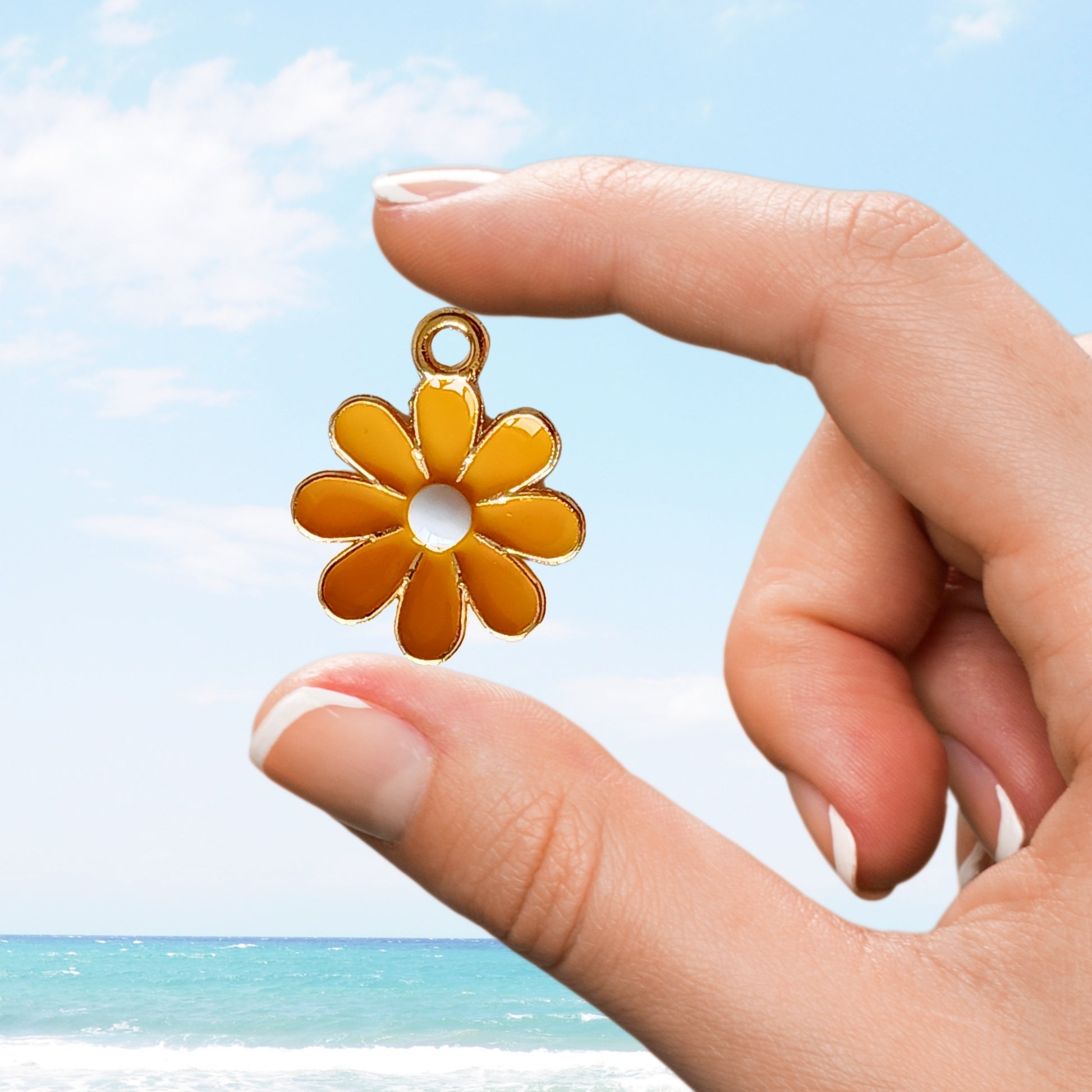 Vibrant orange enamel daisy flower charm with gold outline held by hand
