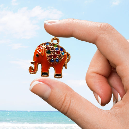Hand holds orange elephant charm with multicolour rhinestones near ocean
