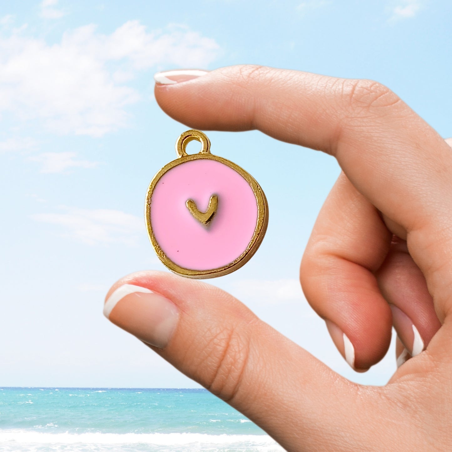 Hand holds round pink charm with gold heart imprint near ocean