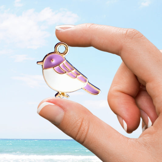 Purple and white bird enamel charm held delicately between fingers