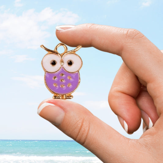 Purple owl charm held between fingers against an ocean backdrop