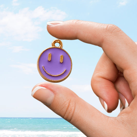 Close-up of a purple smiley face charm held up by hand on a beach
