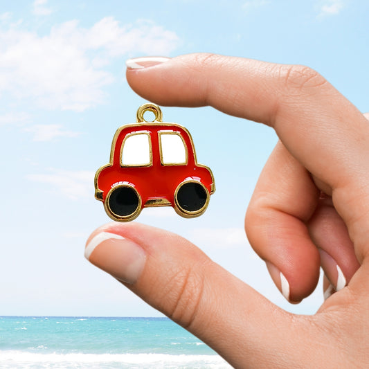 Red enamel car charm with gold outline, held between fingers in front of the ocean.
