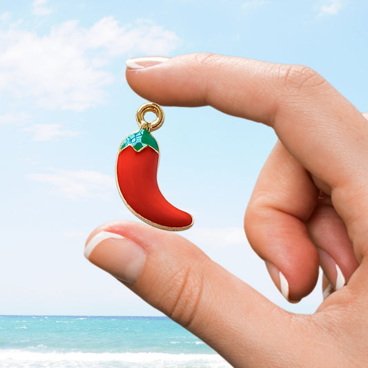 Hand holding a bright red chili pepper enamel charm with gold trim.