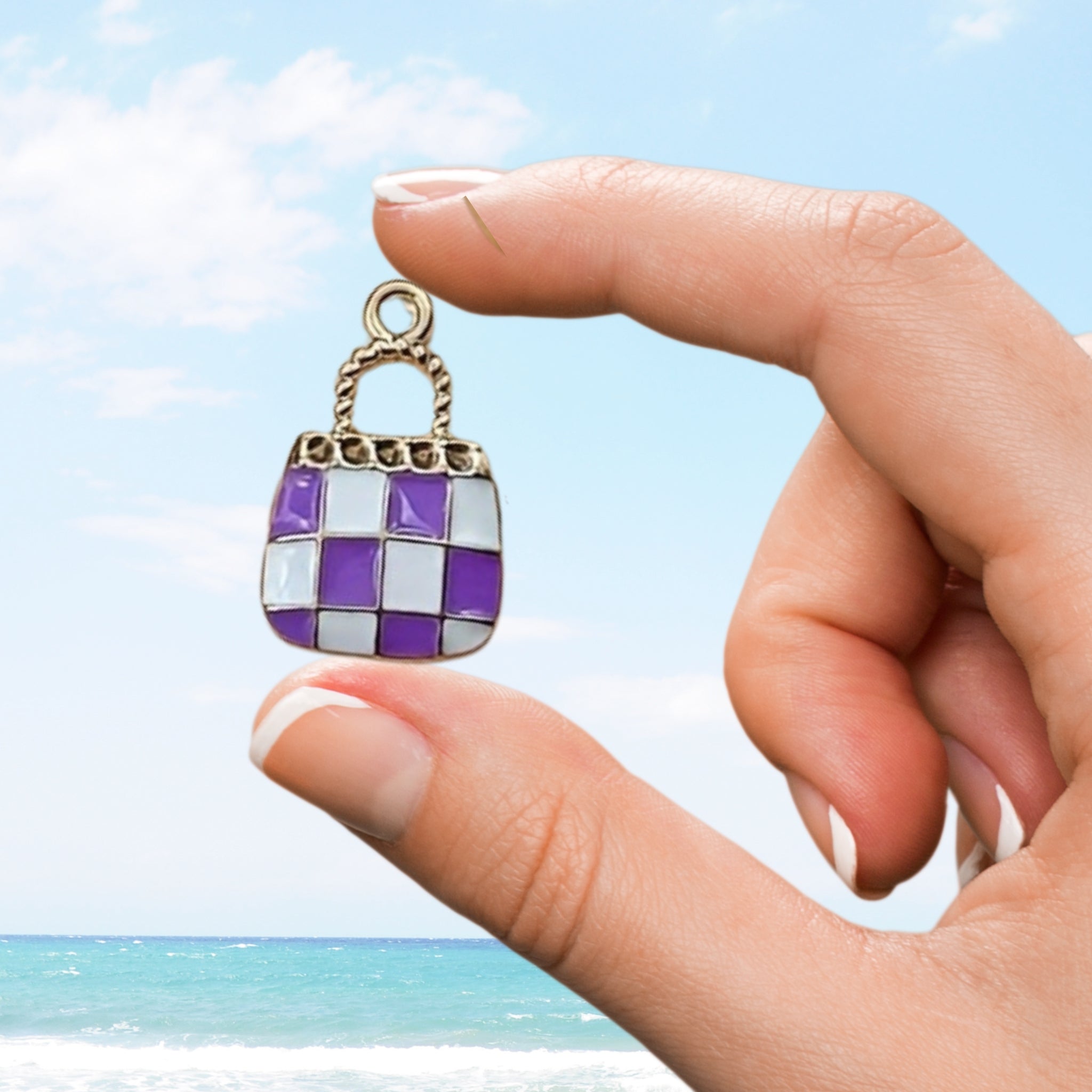 Hand holding small enamel charm of a purple handbag