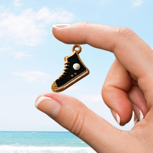Hand holding a black high-top sneaker charm with gold and white detailing by the ocean