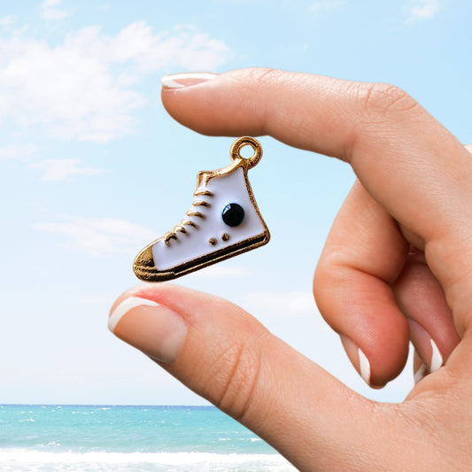 Hand holding a white high-top sneaker charm with black dot details over a beach scene